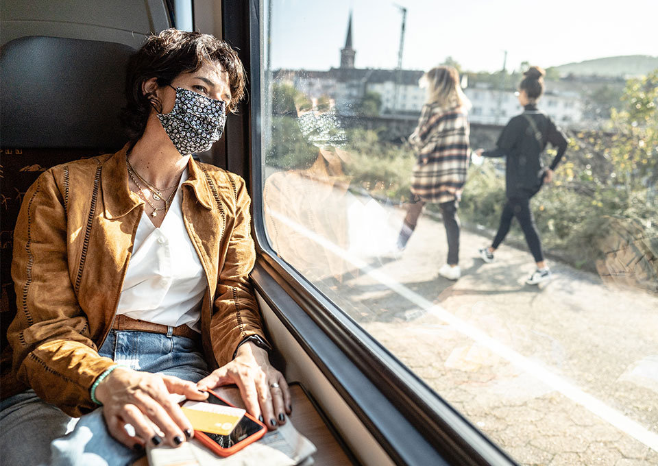 [Translate to English:] Eine Frau sitzt mit Maske im Zug und schaut aus dem Fenster