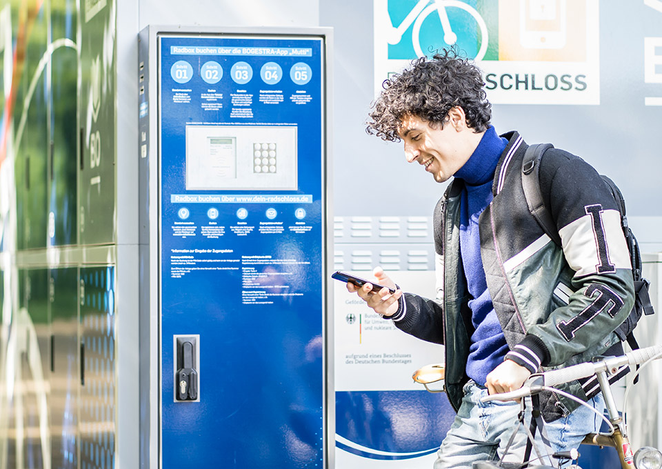 Ein Radfahrer steht mit seinem Smartphone in der Hand an einer Abstellbox von DeinRadschloss