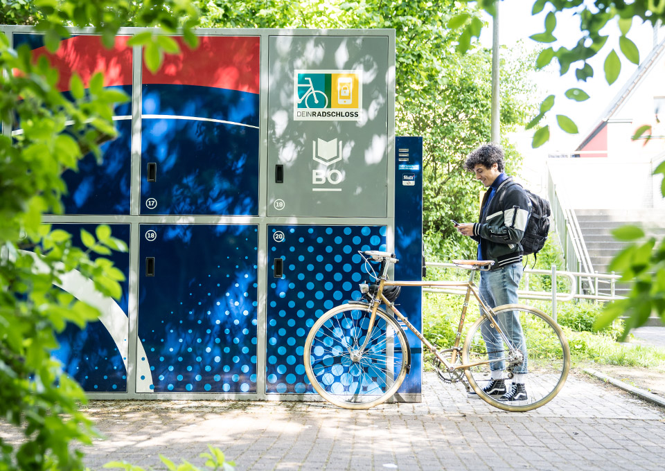 Ein Radfahrer steht mit seinem Smartphone in der Hand an einer Abstellbox von DeinRadschloss