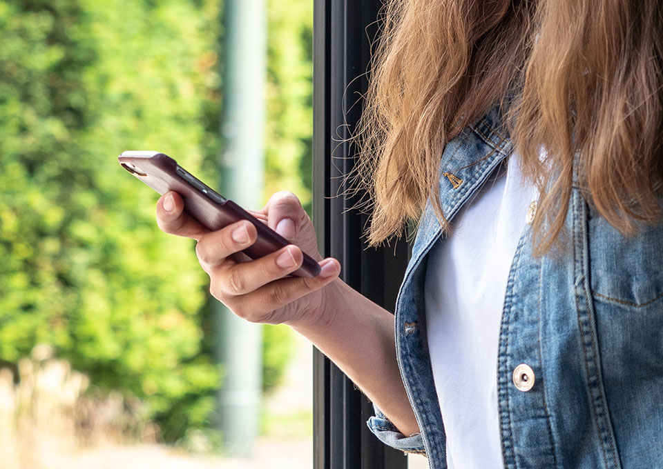 Eine Frau steht in einem öffentlichen Verkehrsmittel vor einem Fenster und hält ein Smartphone in der Hand