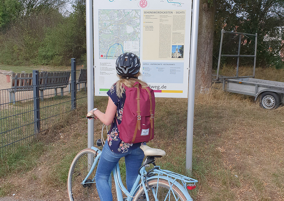 Eine Frau steht mit ihrem Fahrrad vor der Infotafel über den Ruhrtalradweg