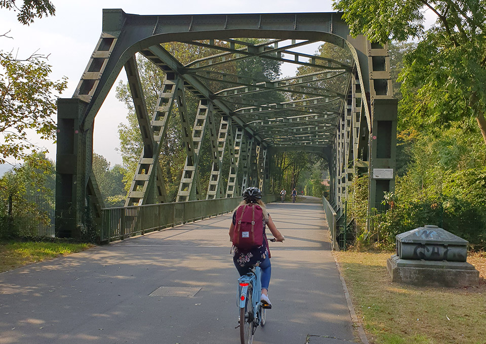 Eine Frau radelt mit ihrem Fahrrad über eine Brücke