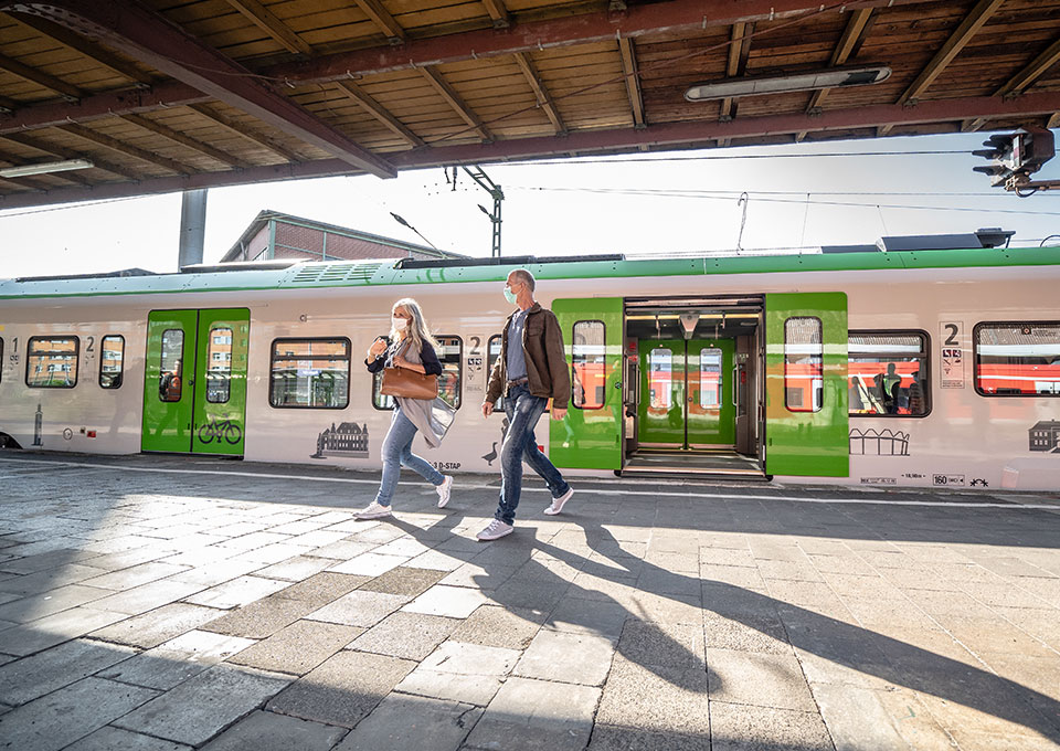 Fahrgäste, die eine Maske tragen, steigen am Bahnhof aus einem Zug aus