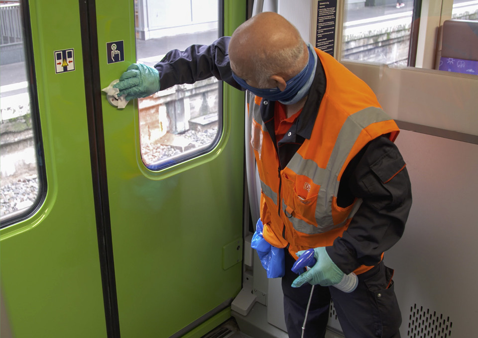 Ein Reinigungsmitarbeiter desinfiziert den Türknopf im Zug