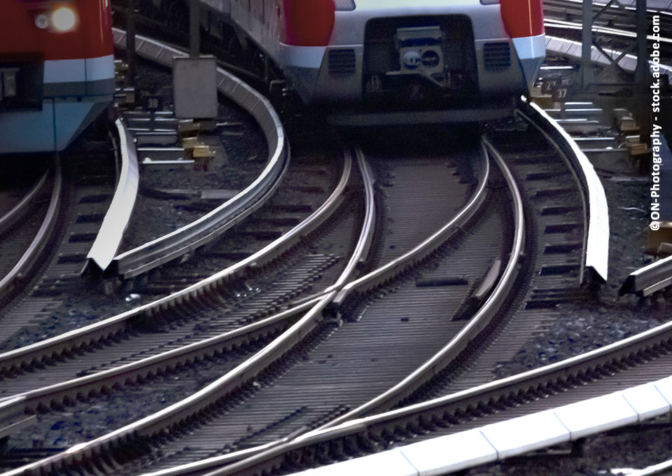 Gleise, auf denen ein Zug fährt, der perspektivisch nur zum Teil zu sehen ist