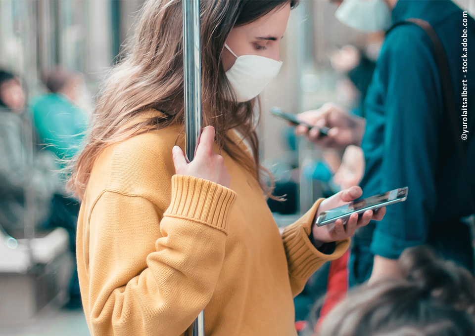Eine junge Frau steht in der Bahn und schaut auf ihr Smartphone