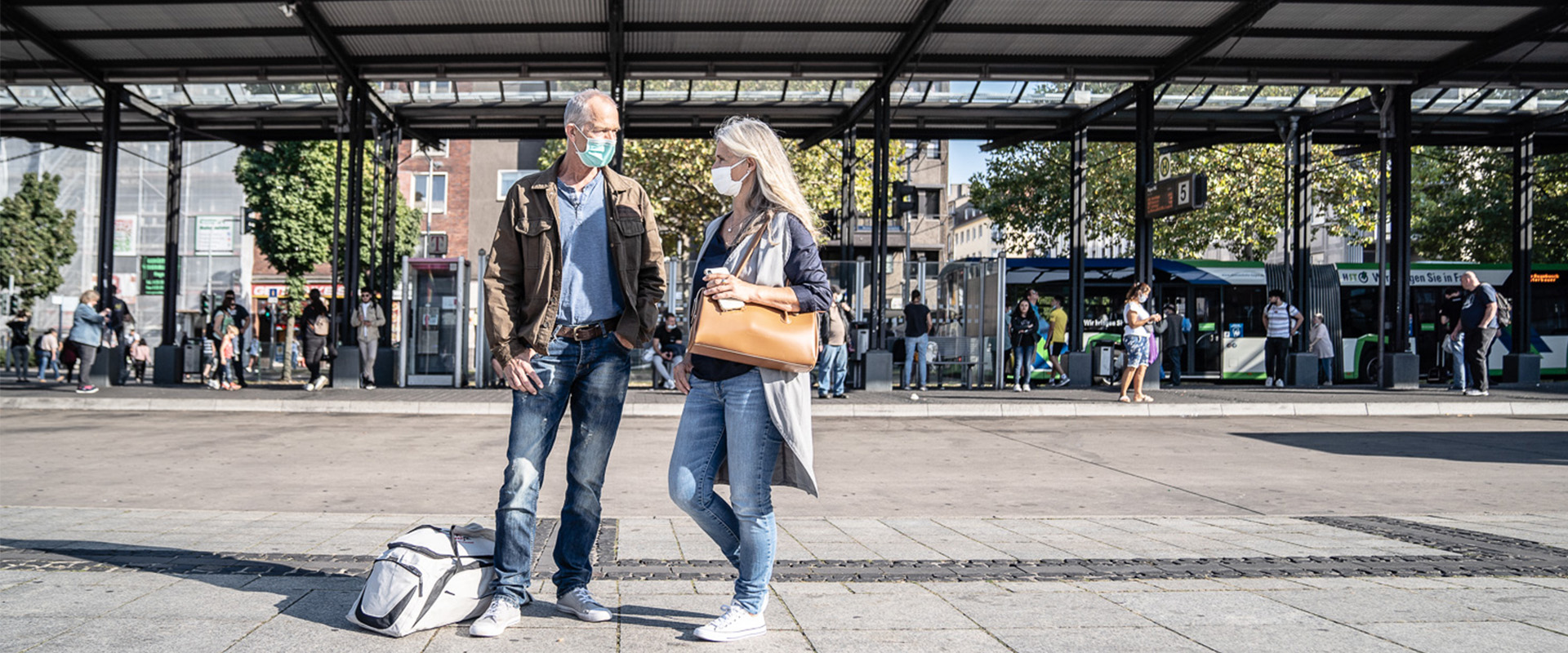 Frau und Mann mit Maske stehen vor Bushaltestellen