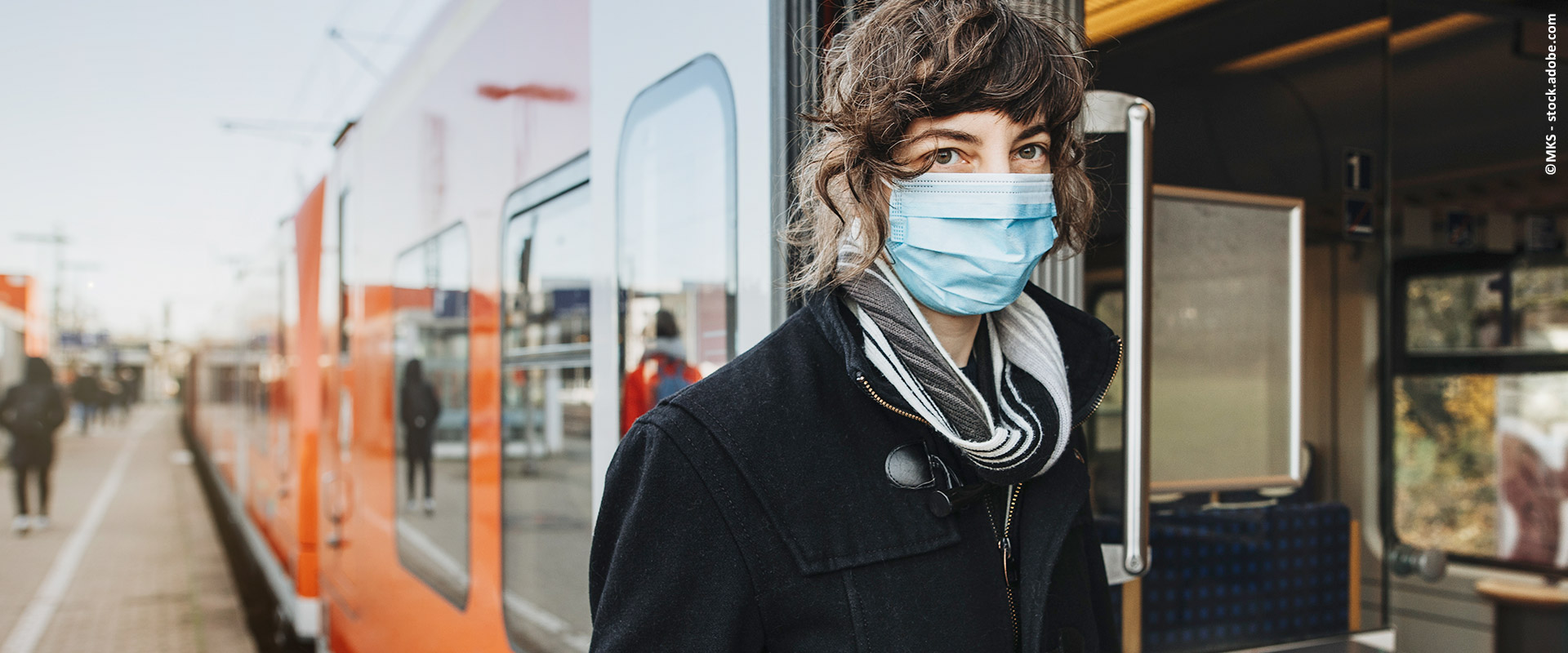 Frau mit Maske steht in der Tür einer am Bahnsteig stehenden S-Bahn