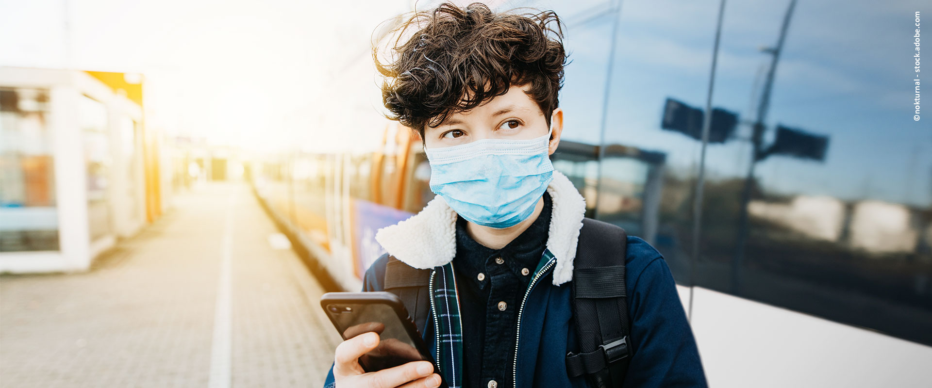 Eine Frau mit Maske und Handy steht am Bahnsteig