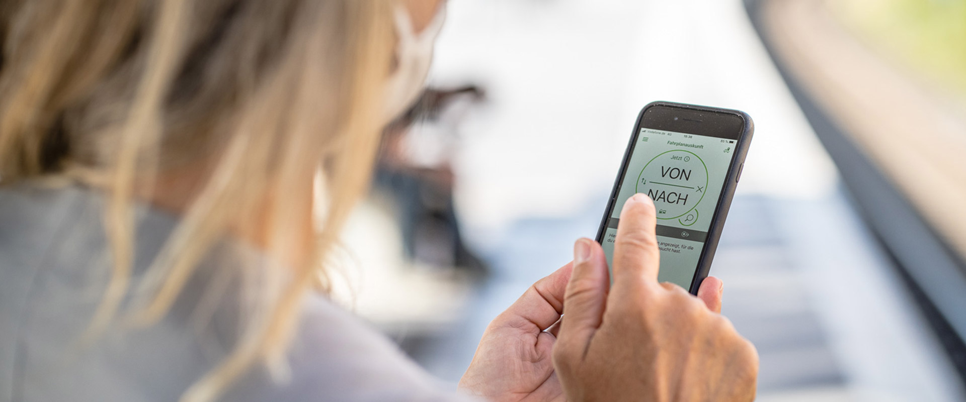 Frau schaut auf ihr Smartphone, auf dem die Verbindungssuche in der VRR App zu sehen ist.