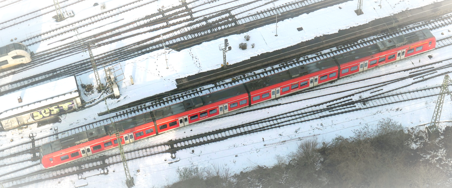 Luftaufnahme einer Regionalbahn auf verschneiten Gleisen