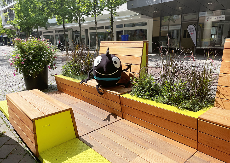 EMW-Maskottchen Edgar sitzt auf einer Stadt-Terrasse