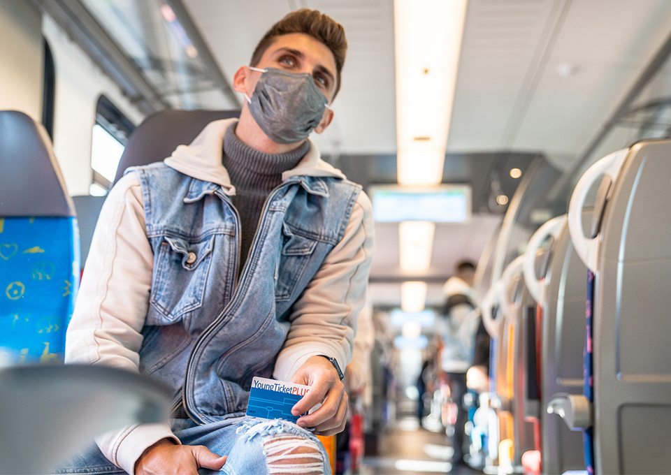 Ein junger Mann sitzt in der Bahn, in seiner Hand hält er das YoungTicketPLUS