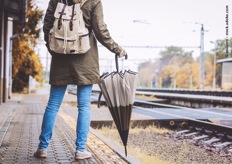 Frau mit Regenschirm wartet am Bahnsteig