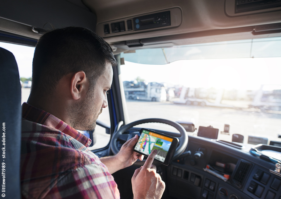 Fahrer am Steuer eines parkenden Lkw mit einem Navigationsgerät in der Hand