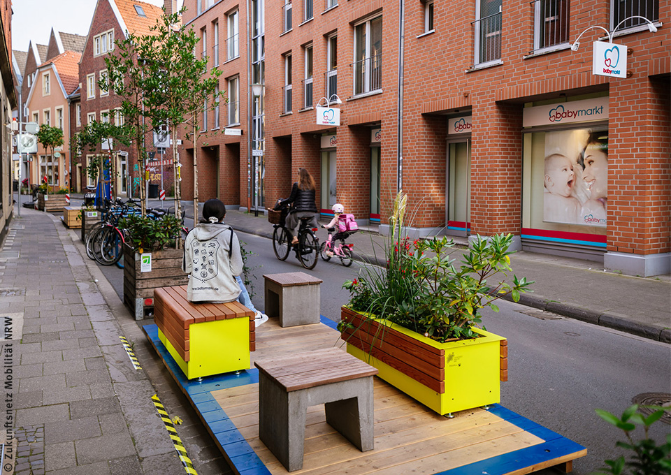 Sitzgelegenheiten am Straßenrand, im Hintergrund Fahrradfahrer