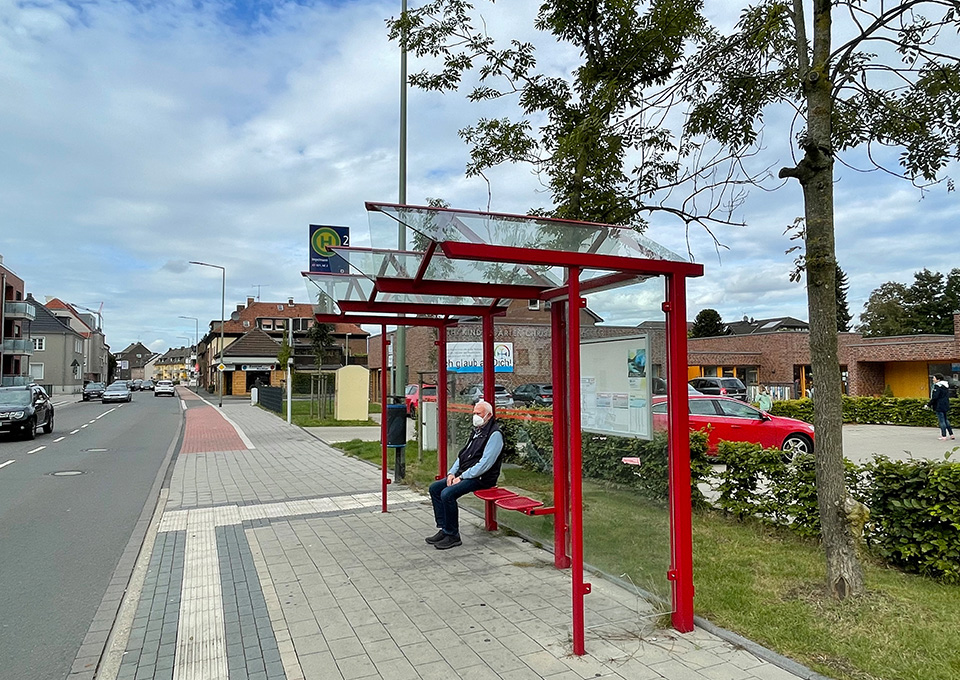 Seitenansicht einer modernisierten Bushaltestelle mit älterem Fahrgast mit Maske