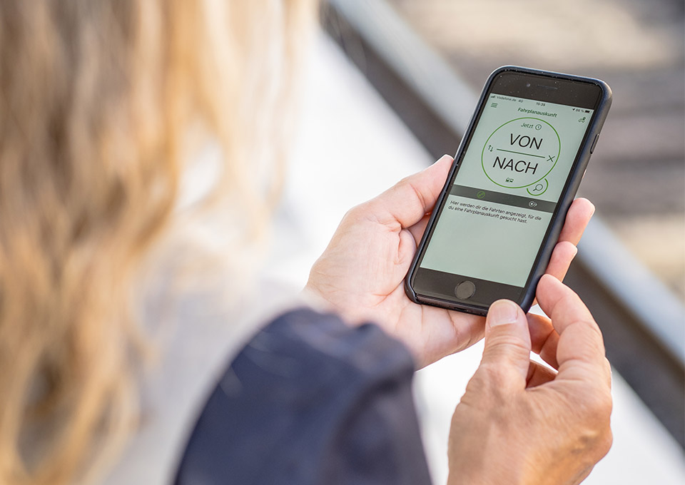 Blick über die Schulter einer Frau auf ein Smartphone mit der VRR App im Display