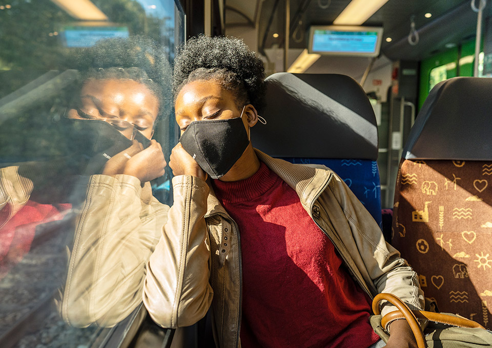 Schlafende Frau mit Maske auf einem Fensterplatz im Zug
