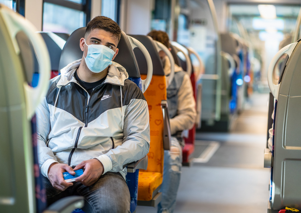 Ein junger Mann mit Gesichtsmaske sitzt in einer S-Bahn