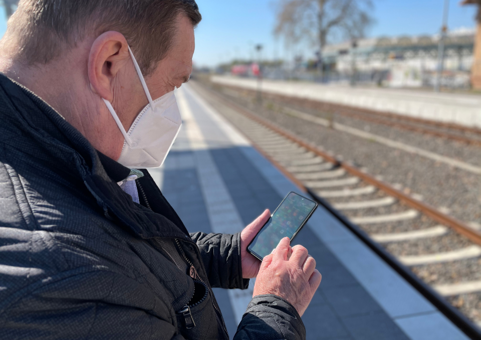 Ein Mann steht am Bahngleis und schaut auf sein Smartphone