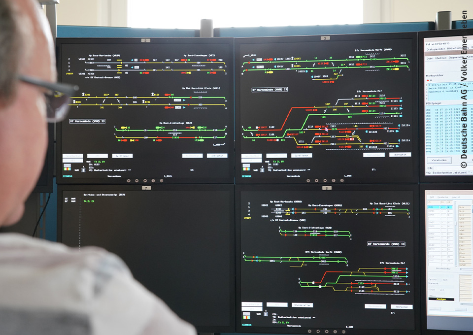 Mann blickt auf Bildschirme in einem Stellwerk