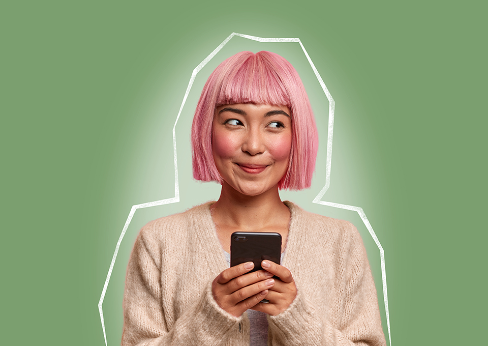 Eine jüngere Frau mit rosafarbenem Haar hält ihr Smartphone in der Hand und blickt erfreut zur Seite