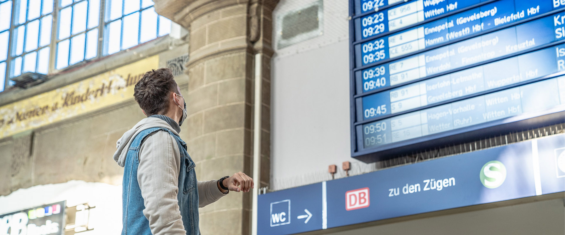 Eine Person blickt an einem Bahnhof auf einen Fahrgastinformationsanzeiger