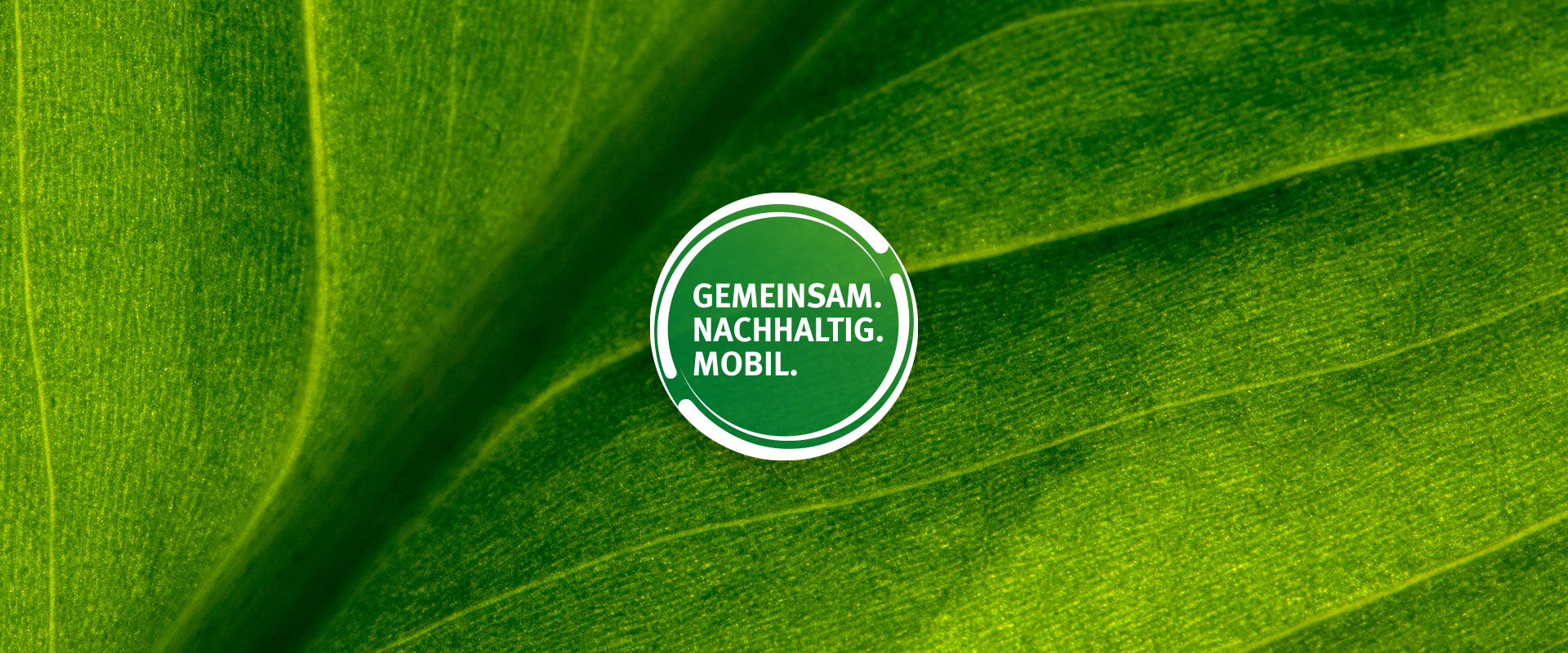 Das kreisförmige Signet "Gemeinsam. Nachhaltig. Mobil.", im Hintergrund eine Detailaufnahme eines grünen Blattes einer Pflanze