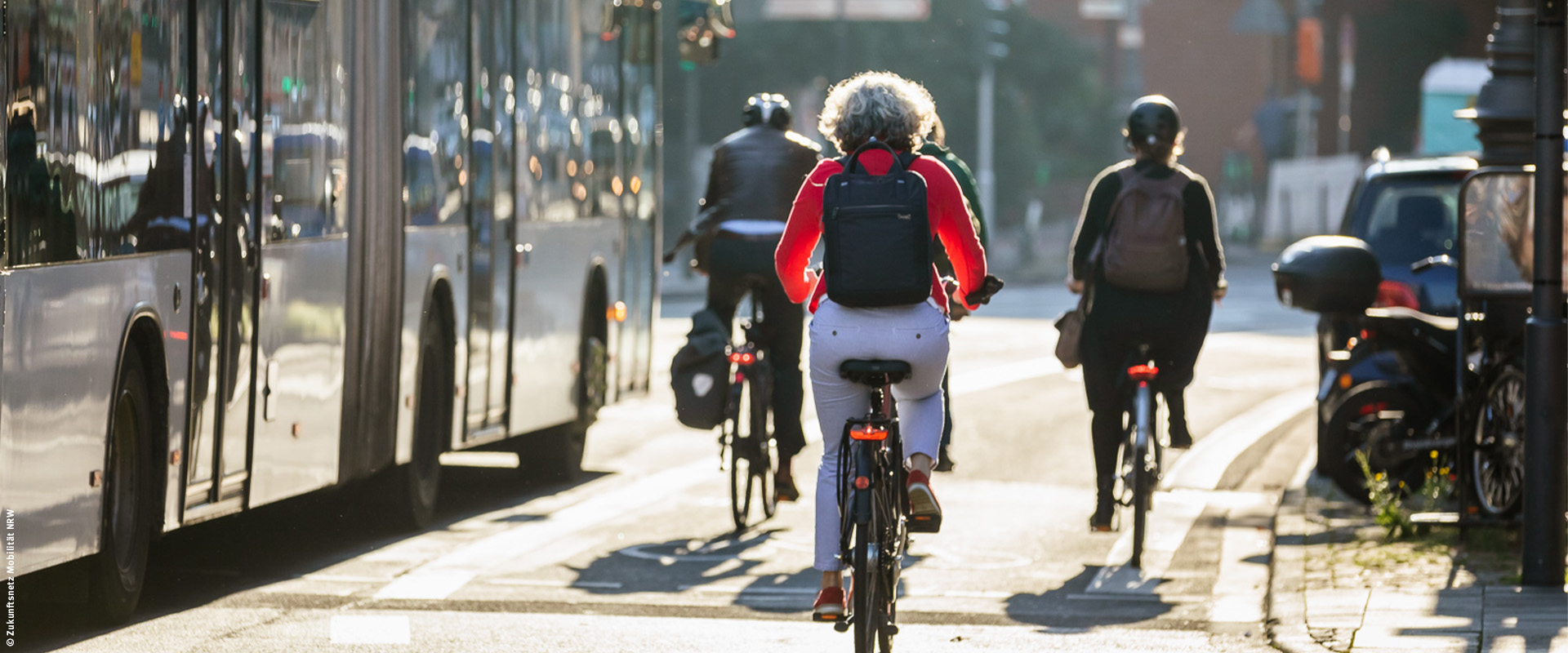 Zukunftsnetz Mobilität NRW Drei Fahrradfahrer*innen fahren neben einem Bus über eine Straße.