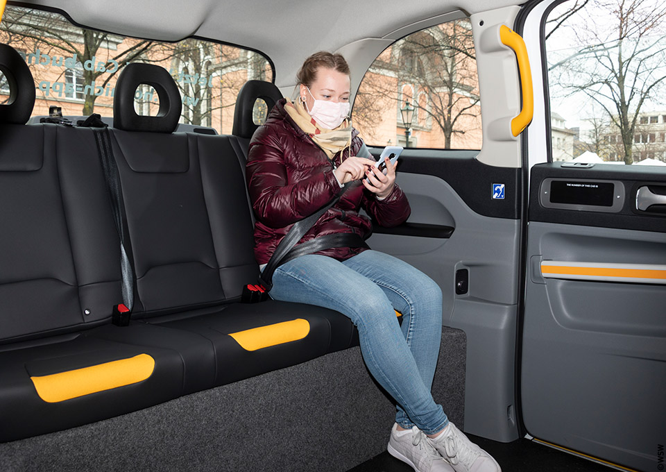 Eine junge Frau sitzt in einem "WSW Cabs"-Fahrzeug und tippt auf ihr Smartphone