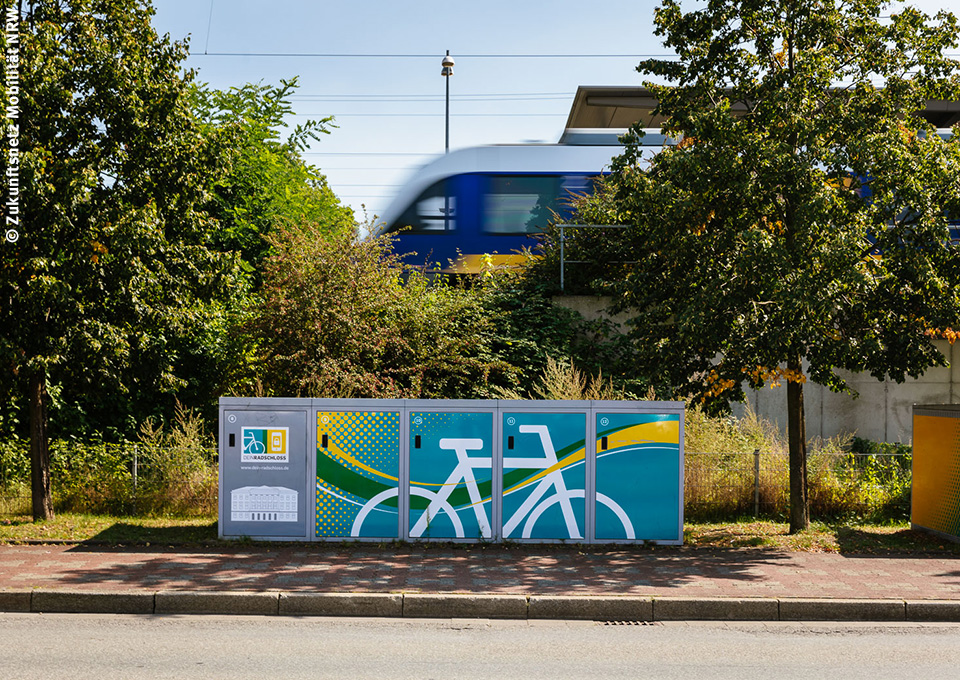 Im Vordergrund sind DeinRadschloss-Boxen zu sehen, im Hintergrund ein Regionalzug