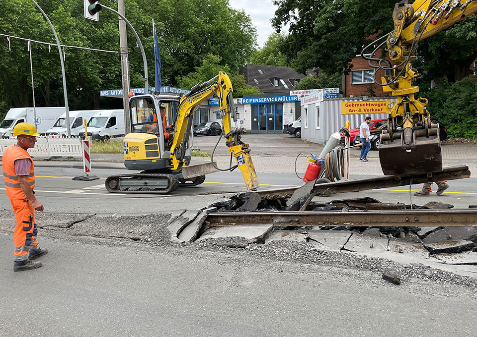 Neubau Haltestelle Brückelstraße: Zwei Baumaschinen nehmen alte Gleise auf, ein Bauarbeiter beobachtet die Arbeiten