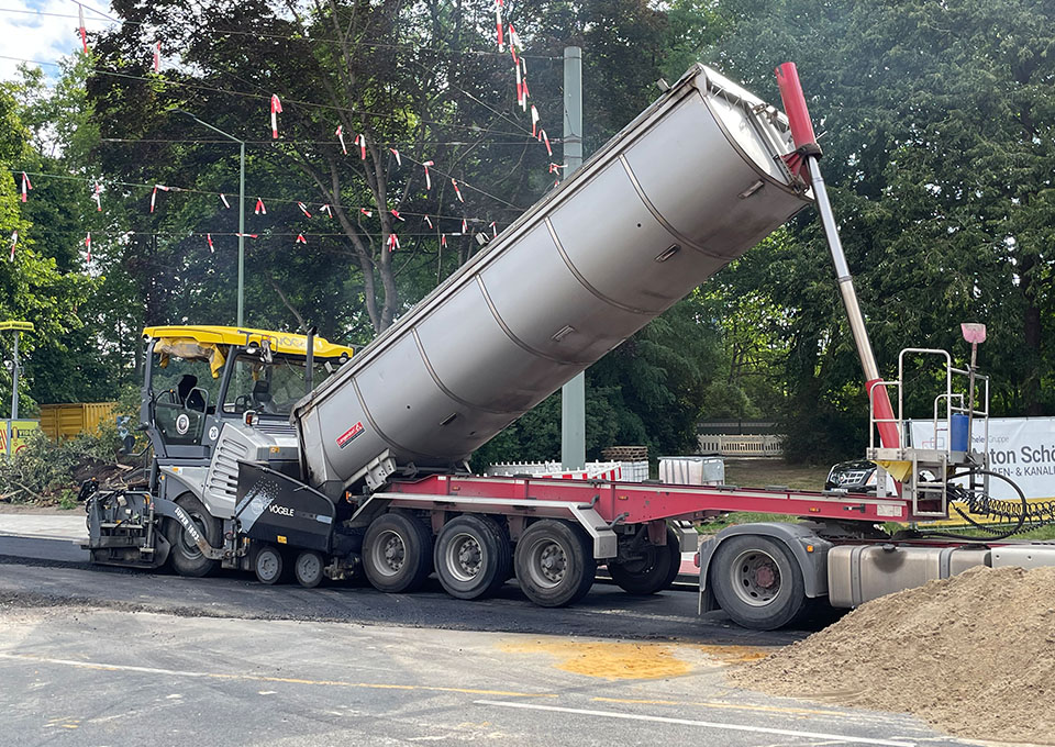 Neubau Haltestelle Brückelstraße: Asphaltierarbeiten, eine Baumaschine und ein Kipplaster sind zu sehen