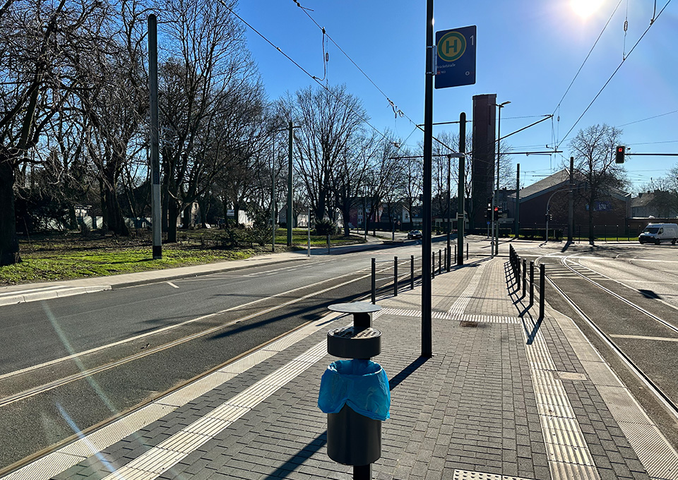 Neubau Haltestelle Brückelstraße: Blick auf einen Teil des fertigen Bahnsteigs mit der Rampe im Hintergrund, zu sehen ist ein Mülleimer, ein Haltestellenschilt und taktile Leitelemente