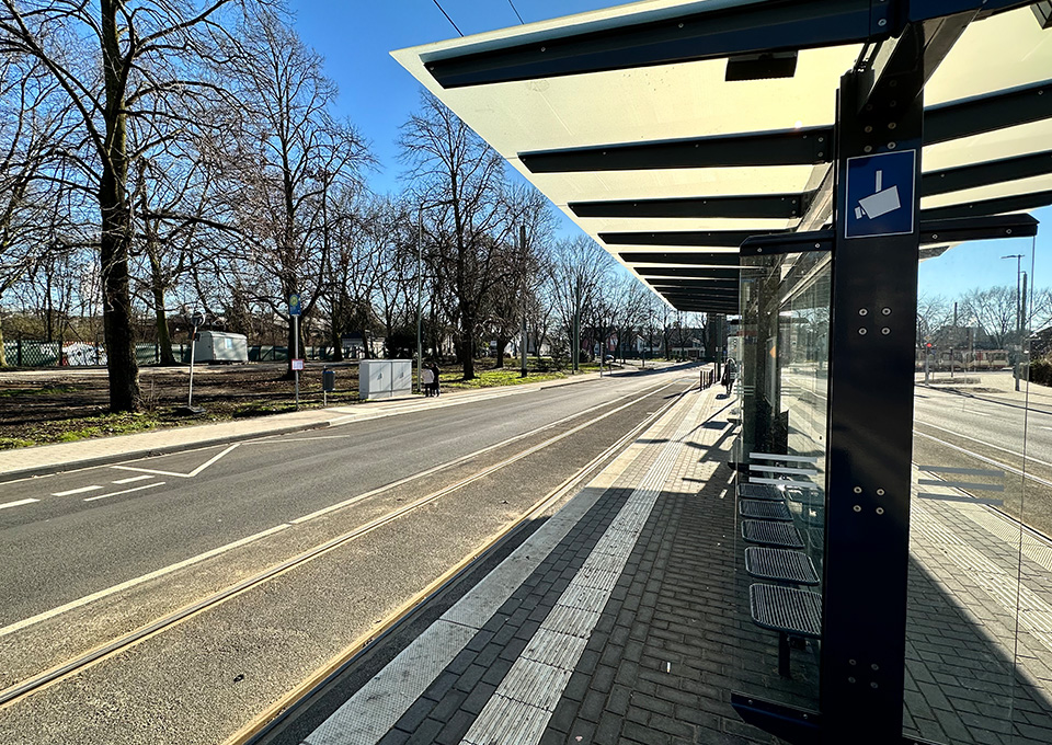 Neubau Haltestelle Brückelstraße: Blick auf die fertige Haltestelle mit Wetterschutz, Sitzgelegenheiten und einem Hinweisschild auf Videoüberwachung, im Hintergrund ist ein Fahrgast zu sehen