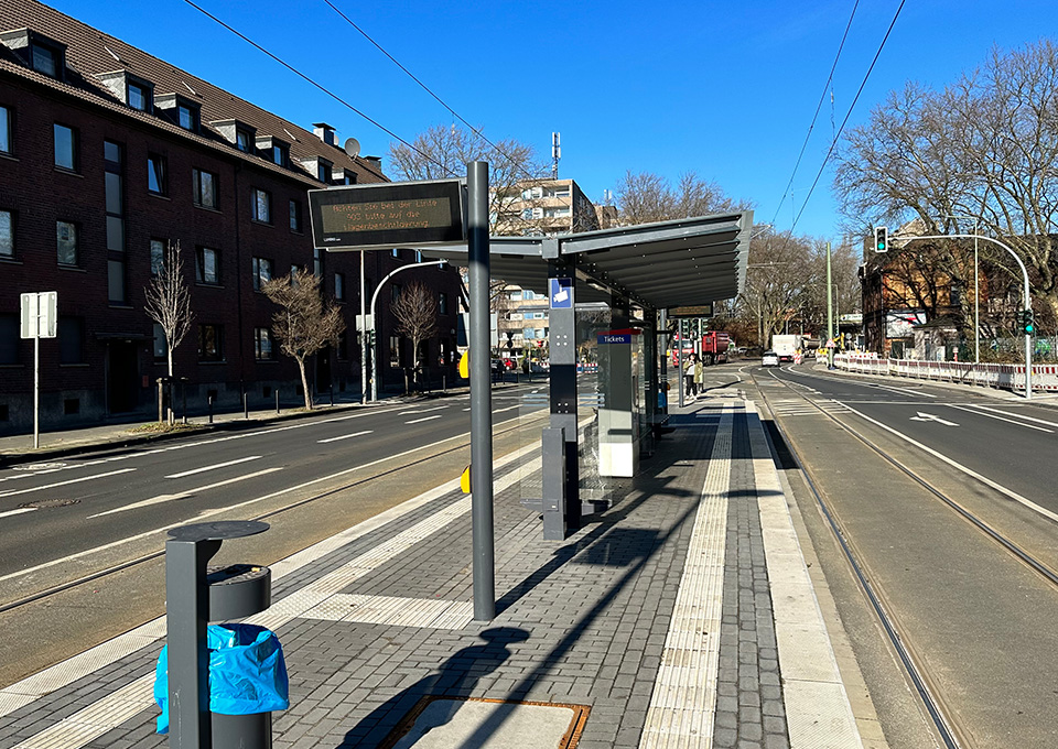 Neubau Haltestelle Brückelstraße: Blick auf die fertige Haltestelle mit Wetterschutz, dynamischen Fahrgastinformation, Mülleimer, Ticketautomat und Sitzgelegenheiten, im Hintergrund ist ein Fahrgast zu sehen