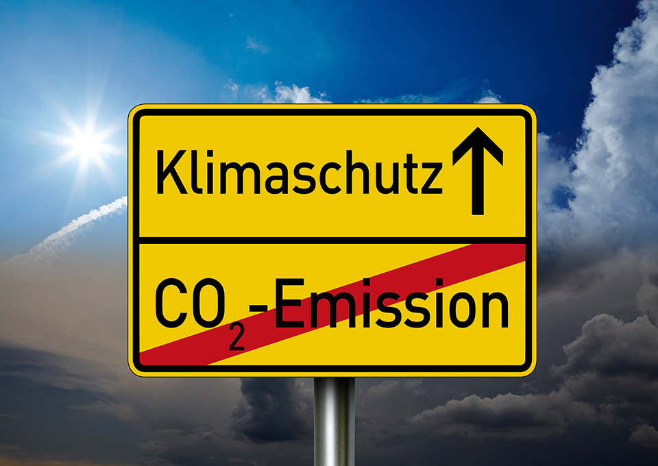 Gelbes Schild, unten ist rot durchgestrichen "CO2-Emission" zu lesen, oben mit einem Pfeil nach oben "Klimaschutz"
