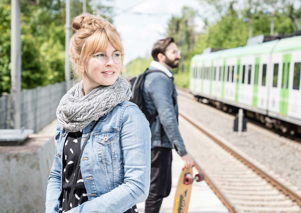 Zwei Personen stehen am Bahnsteig. Im Hintergrund ist eine S-Bahn zu sehen