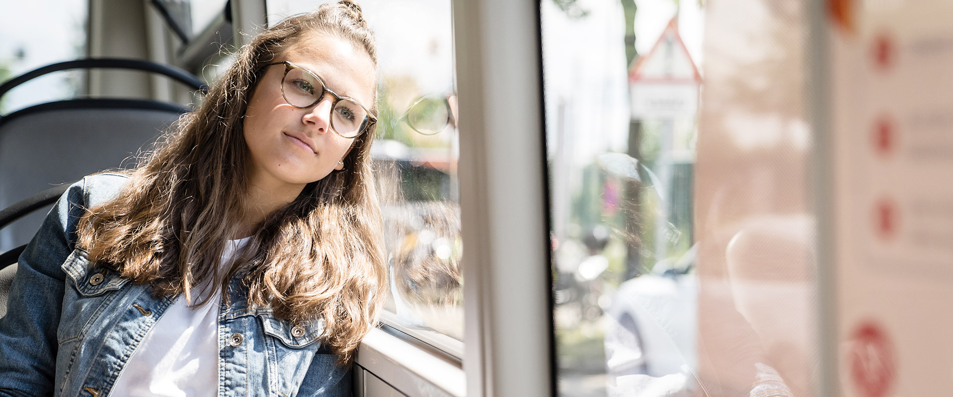 Eine junge Frau mit Brille in einem Bus sitzend. Sie lehnt ihren Kopf an die Scheibe.